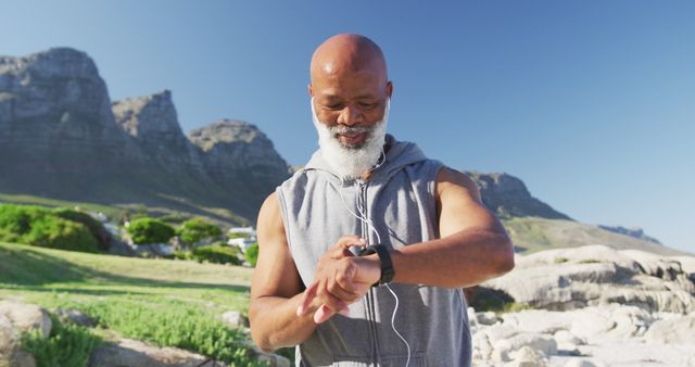 Senior man checking his smartwatch while working out in a mountainous outdoor environment. Perfect for illustrations of fitness, active senior lifestyles, outdoor exercise, and wearable technology.