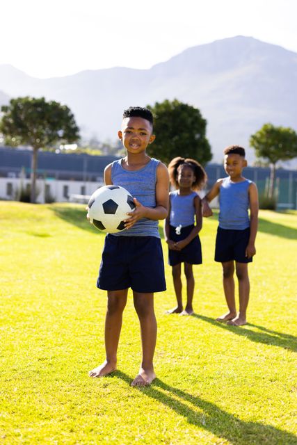 Three happy african american boys and girls with football in elementary school playing field. Education, health, childhood and learning concept.