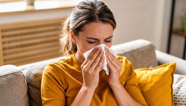 Woman blowing nose on couch with tissue for cold allergy relief and home wellness