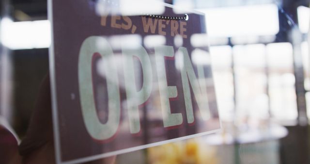 Close-up of a shop's open sign hanging on a glass door, conveying business hours or reopening. Ideal for use in articles about small businesses, entrepreneurship, business hours, reopening after lockdowns, and marketing for physical retail stores.