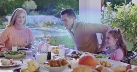 Family enjoying outdoor autumn dinner on porch with roast chicken and pumpkin centerpiece