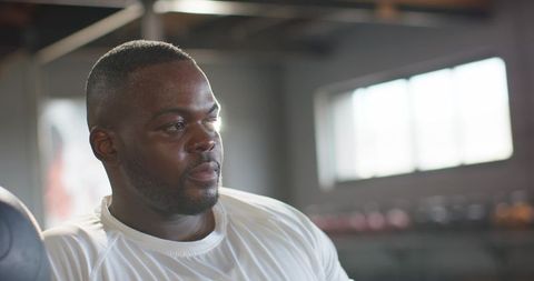 African man recovering after intense workout holding medicine ball in backlit gym studio