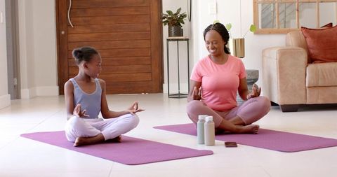 Mother and daughter practicing meditation on purple yoga mats at home for family wellness