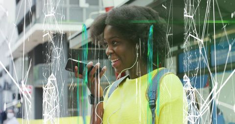 An African American woman is engaged in a lively conversation on her smartphone while wearing headphones. An abstract digital overlay of white and green patterns adds a dynamic and futuristic element to the scene. This visual can be used in technology advertisements, communication concepts, or urban lifestyle promotions, highlighting the merging of real-world interactions with digital interfaces.