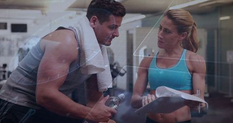 Female personal trainer coaching male client with clipboard and water bottle in modern gym
