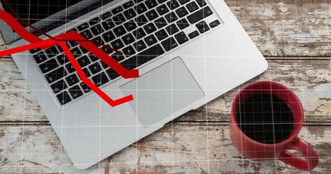Silver laptop with red downward arrow graph on rustic wooden desk with red coffee mug