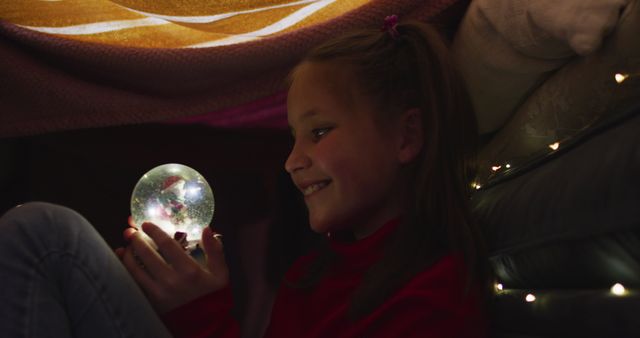 Young girl enjoying time inside homemade fort, holding glowing crystal ball. Useful for themes related to childhood imagination, playing, adventure, and indoor activities. Ideal for advertising children’s toys, creative playtime, and family bonding opportunities.