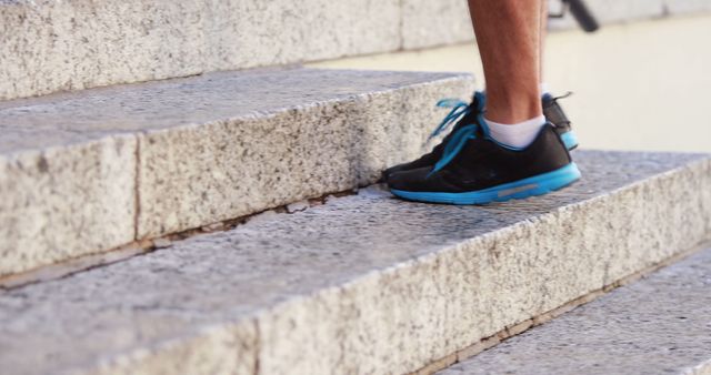 This image depicts the legs of a runner in black and blue sneakers climbing outdoor stairs. Ideal for use in discussions about fitness routines, exercise tips, running, sports gear advertising or health and wellness blogs.