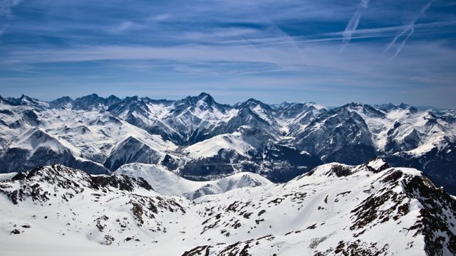 Panoramic aerial view of majestic snow-capped mountains under a vibrant blue sky. Excellent for travel brochures, winter sports promotions, or websites showcasing natural landscapes. The image highlights the pristine beauty of high-altitude environments, inviting viewers to explore the vastness and tranquility of these snowy ranges.