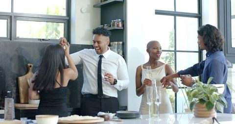 African american friends celebrating at modern kitchen island clinking champagne flutes