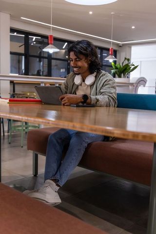 Indian man working on tablet in modern coworking space wearing headphones