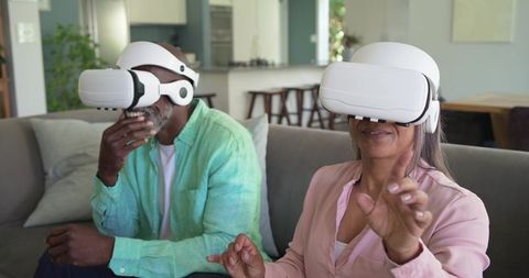 Mature diverse couple exploring virtual reality at home, woman reaching forward