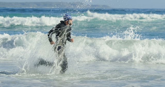 A middle-aged Caucasian man in a wetsuit is running through the surf on a beach, with copy space. His dynamic movement suggests he is either entering or exiting the water, partaking in water sports activities.