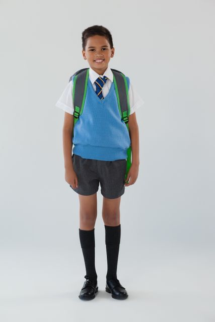 Young boy in school uniform standing with a backpack, smiling confidently. Ideal for educational materials, school advertisements, and back-to-school promotions.