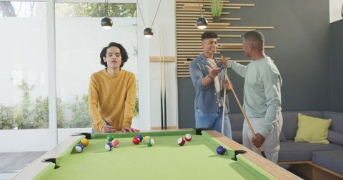 Diverse friends playing pool in modern game room socializing around green billiards table