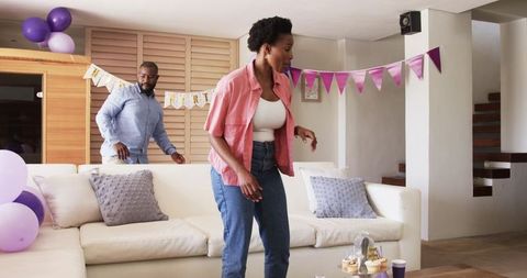 African American couple decorating living room for cozy party with balloons and cupcakes
