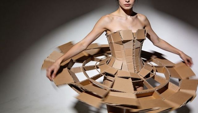 Spinning model wearing sculptural cardboard corset with circular ringed skirt eco couture