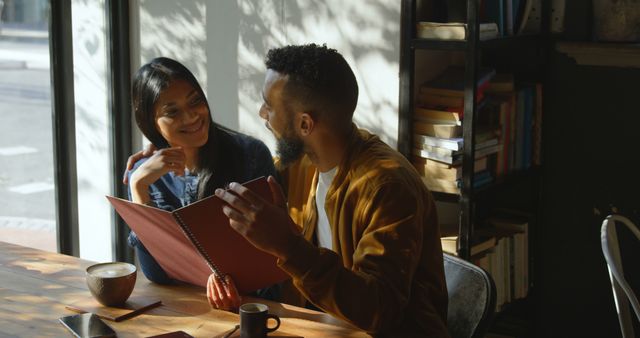 A young man and woman enjoying coffee and chatting at a cozy café. Sunlight pours through large windows, creating a warm and inviting atmosphere. Perfect for illustrating moments of connection, relaxation, and leisure in promotional materials for cafés, restaurants, or dating services.