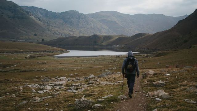 Hiker Walking Toward Mountain Lake in Remote Valley Under Overcast Sky, Backpacking