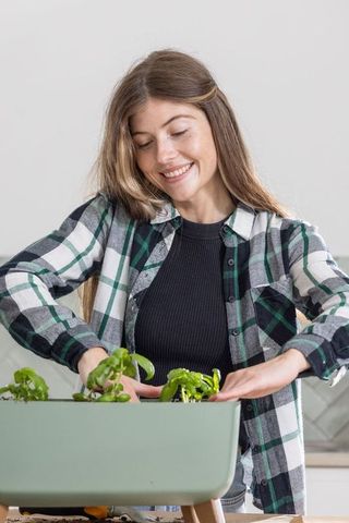 Young woman tending indoor herb planter on stand in modern kitchen, urban gardening lifestyle