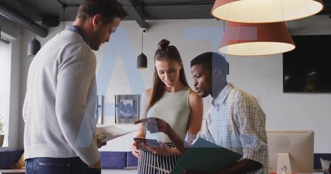 Young professionals collaborating around smartphone and documents in modern office meeting