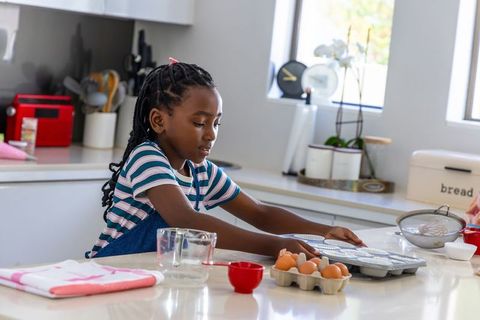 African american girl placing cupcake liners in muffin tin in sunlit modern kitchen