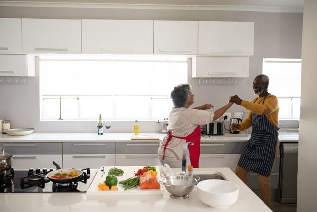 A senior African American couple at home together, social distancing and self isolation in quarantine lockdown during coronavirus covid 19 epidemic, dancing in kitchen.