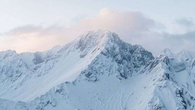 Snowy peak rising above windswept ridgelines with dramatic cornices at sunrise