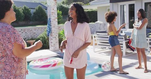 Laughing friends enjoying backyard plunge pool party on sunny patio with colorful float
