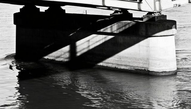 Monochrome high-contrast concrete bridge pier casting diagonal shadows over rippling river
