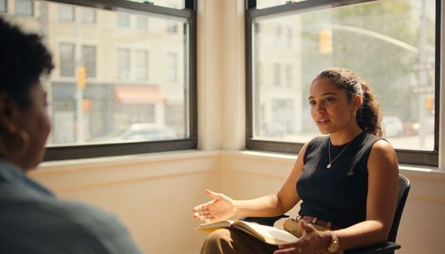 Hispanic woman leading consultation in sunlit urban office corner with notebook