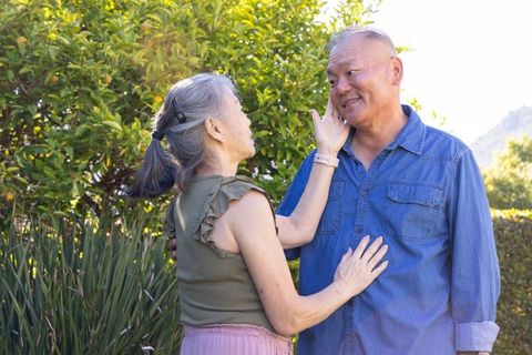 Asian mature couple sharing tender moment in sunlit backyard, woman touching man's cheek