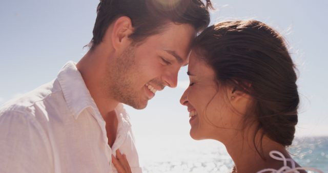 A young Caucasian couple shares a tender moment, with copy space. Their close proximity and joyful expressions suggest a romantic connection against a bright, sunlit backdrop.