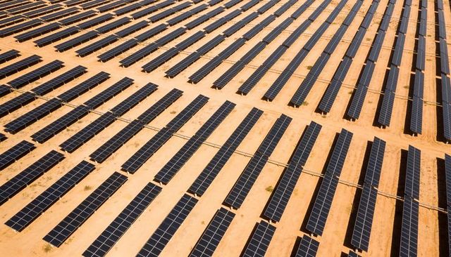 Aerial showing vast solar farm forming parallel rows of photovoltaic panels on desert