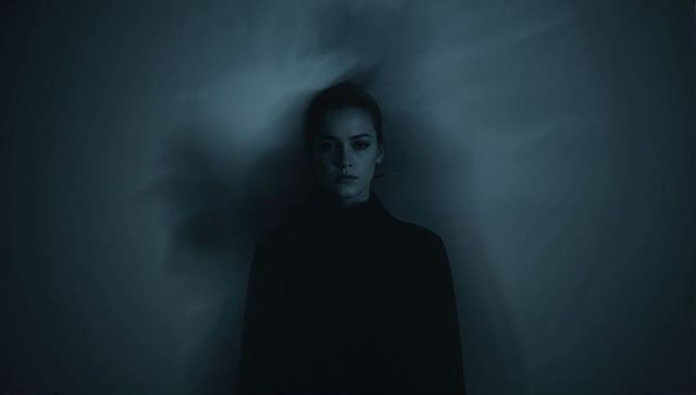 Posing female model wearing high-neck dark top showing halo shadow with moody lowkey light