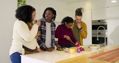Diverse friends cooking together in modern kitchen prepping colorful vegetables at island