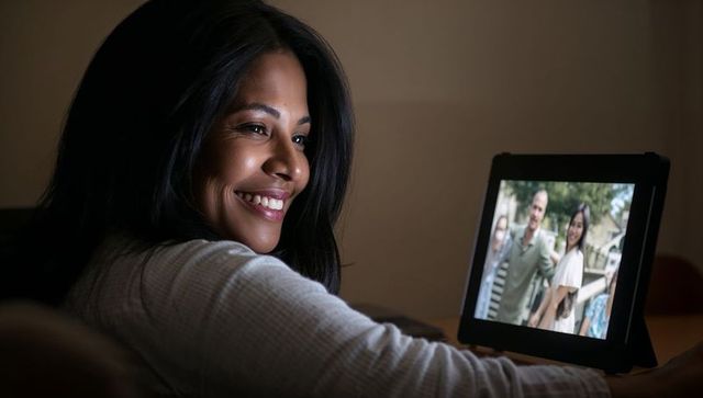 Smiling woman reaching toward tablet during video chat, cozy evening warm ambient light