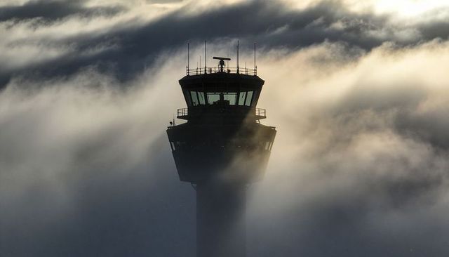 Airport control tower piercing low fog with backlit radar dome and green-tinted cab