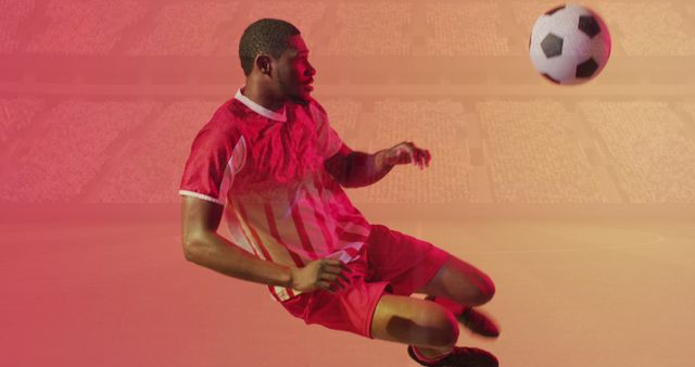 Shows an athlete in mid-air kicking a soccer ball in a stadium surrounded by a red hue. Ideal for use in sports promotions, advertisements for athletic apparel, and content emphasizing teamwork and competition. Can also be used in articles related to soccer or professional sports.