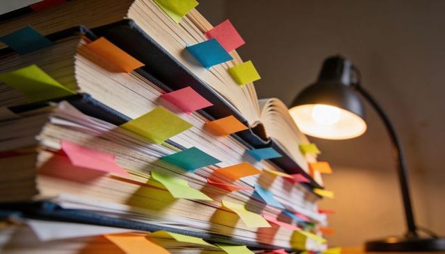 Organizing notes using colorful sticky tabs in open textbooks under warm desk lamp