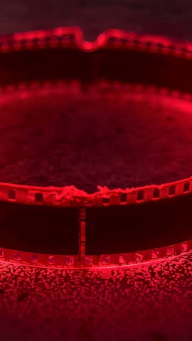 Shifting focus on 35mm film loop glowing red revealing splice and torn perforations