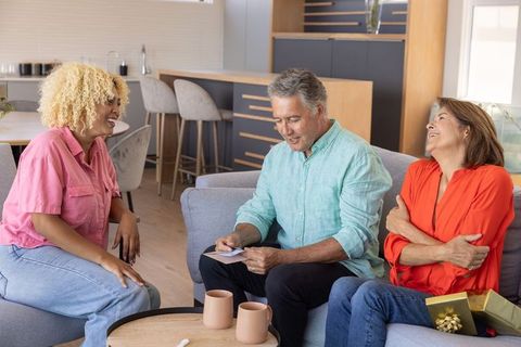 Multigenerational friends celebrating gift and reading card in bright modern living room