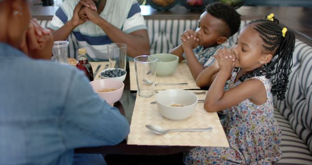 Happy african american parents, brother and sister saying prayer with eyes closed at family meal. Family, religion, prayer, meal, childhood and domestic life, unaltered.
