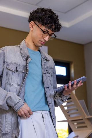 Young asian man using tablet in minimalist interior wearing denim jacket and glasses