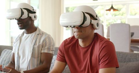 Diverse male friends playing VR games on couch wearing headsets and holding controllers