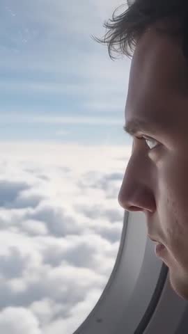 Vertical video of male passenger gazing through airplane window at clouds and horizon