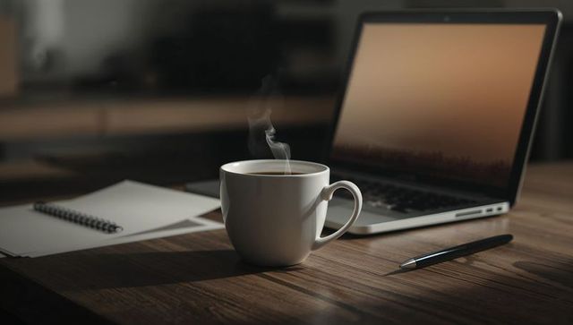 Steaming coffee mug on wooden desk with laptop and notebook for cozy home office workspace