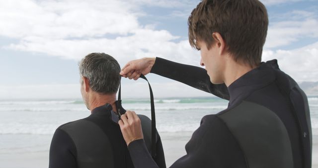 Young Man Helping Senior Man Put On Wetsuit at Beach Under Blue Sky - Download Free Stock Images Pikwizard.com