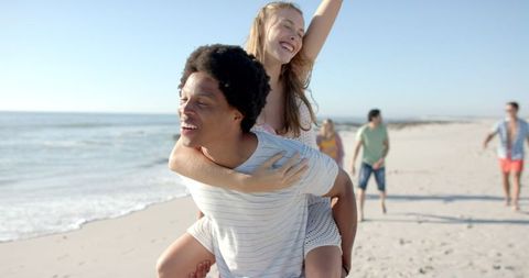 Joyful friends enjoy beach piggyback adventure