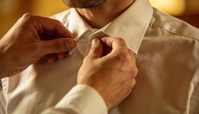 Hands fastening white dress shirt collar on man getting ready for formal event close-up